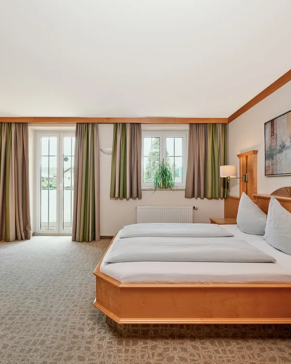 Geräumiges Hotelzimmer mit Doppelbett, Holzmöbeln, Schreibtisch und Tageslicht vom Balkon